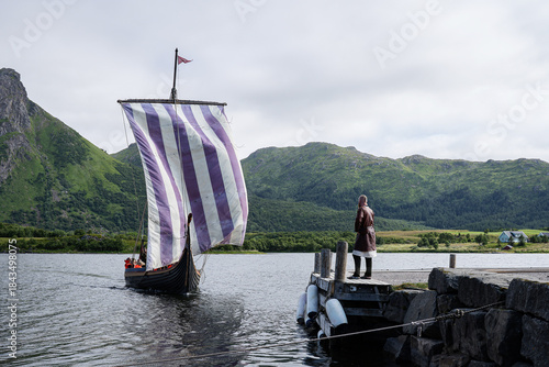 Viking wooden boat arriving on the shore and a waiting man wearing viking clothes at Lofoten islands.