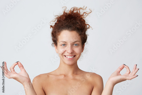 Horizontal shot of happy peaceful yong woman with perfect skin after applying cream or mask shows meditation gesture by hands isolated over white background Feels peaceful and satisfied