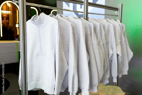 Close-up of white zip-up jackets on black hangers in retail rack