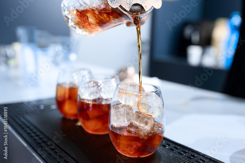 A bartender pours a vibrant pink cocktail through a fine mesh strainer into a stemless wine glass filled with ice