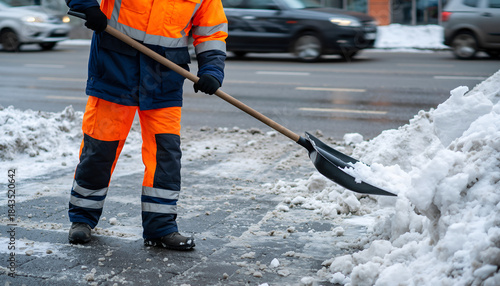 Worker in high-visibility clothing shoveling snow from a sidewalk.