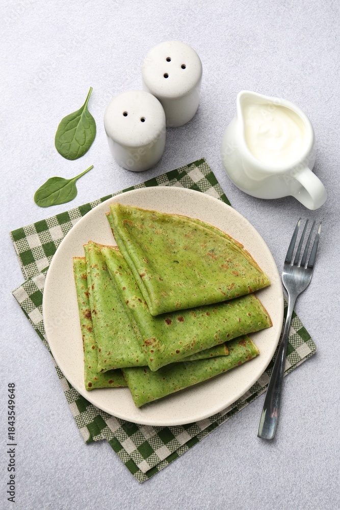 Fototapeta premium Tasty spinach crepes with leaves and sour cream on grey table, flat lay