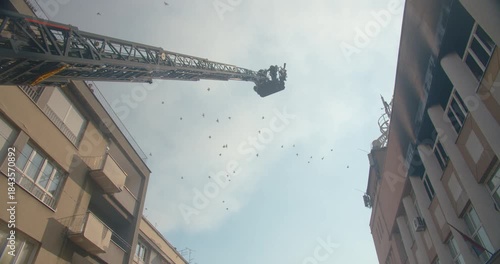 Silhouette of a fireman in a bucket on the ladder of a fire engine lifting into the air into the roof of a burning building