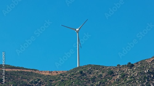 Close up view of wind turbine on rocky mountain slope against clear blue sky on background. Greece.
