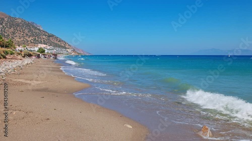 Magnificent view of Aegean Sea waves rolling along pebbled beach with mountains on background. Greece.