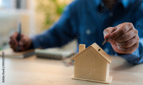 A man hand putting coins into a house bank saving bank for account save money. Planning step up, saving money for future plan, retirement fund. A business investment-finance accounting concept.