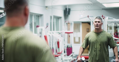 Dumbbell raises for the deltoid muscles. Deltoid workout. Man works deltoids with dumbbell raises in front of the gym mirror, maintaining good form.