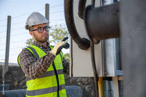 Electrical engineer performing safety inspection on industrial control panel at outdoor power facility site