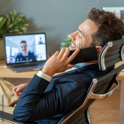 A man in a suit laughs while on a phone call during a video conference meeting.