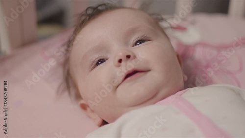 Cute smiling baby girl lying awake in her crib
