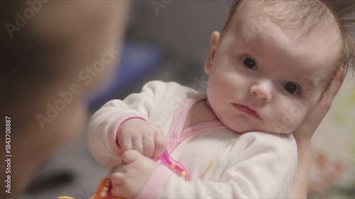Adorable baby girl looking at camera while held in her mother's arms