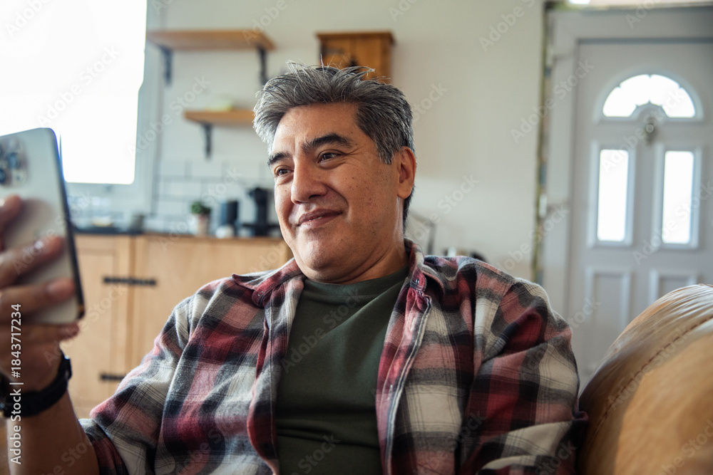 Obraz premium Mature man smiling at smartphone in living room