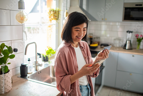 Adult woman smiling making mobile payment in home kitchen