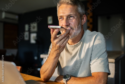 Фотография Mature man using smartphone voice assistant at home, focused