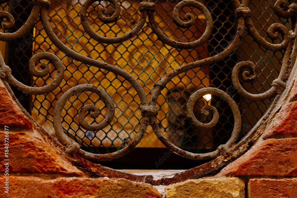 Fototapeta premium Intricate wrought iron grille on vintage brick wall with warm lighting