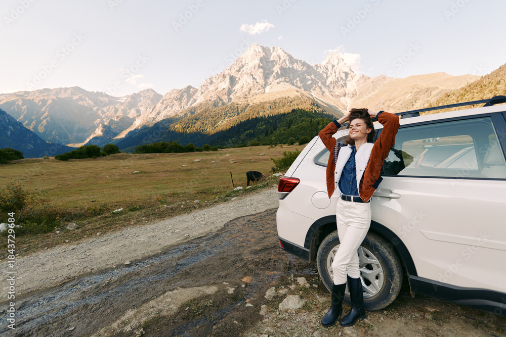 Fototapeta premium Woman, car, mountains, nature, road, travel, landscape, adventure - Young woman leans on white SUV on dirt road by alpine mountains, enjoying outdoor travel, scenic landscape and weekend adventure.