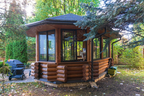 Beautiful log gazebo in a quiet autumn garden surrounded by lush greenery in the afternoon.