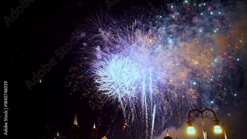 Bright fireworks burst in various colors, illuminating the night sky above a lively city park during an evening festival. Families and friends gather to enjoy the spectacular display together.