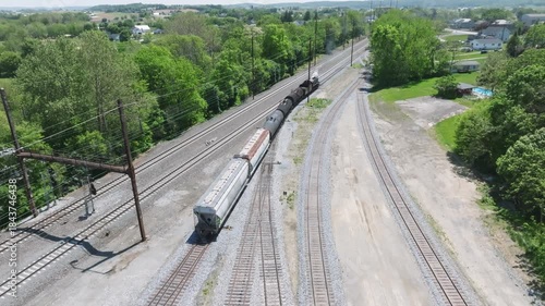 A vintage steam freight train makes its way backing up in yard performing switching operations moving steadily along the railway tracks in a peaceful countryside setting.