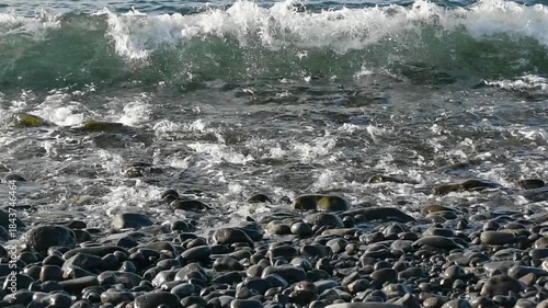 waves of the Atlantic Ocean splashing on a pebble beach in Madeira, Spain