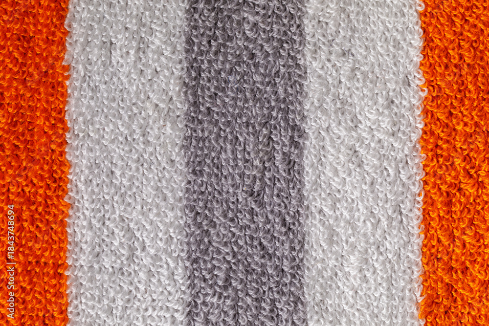 Fototapeta premium A close-up shot of a textured gray towel, with orange and white strips showcasing its fluffy and soft fabric loops.