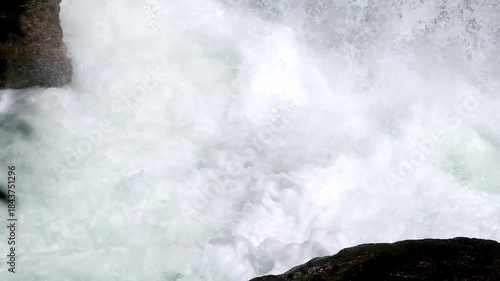 Dramatic waterfall water spray and mist over dark rocks