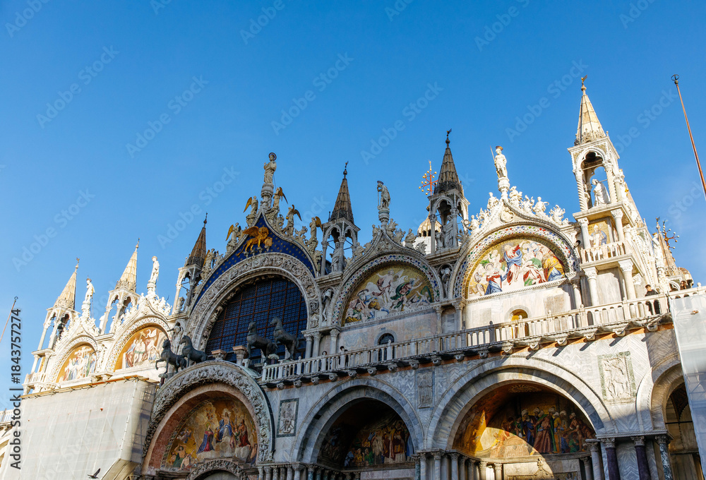 Naklejka premium Venice, Italy - December 05, 2025: St. Mark's Basilica in Venice showcases stunning architecture with intricate sculptures and vibrant mosaics under a clear blue sky, a symbol of historical beauty