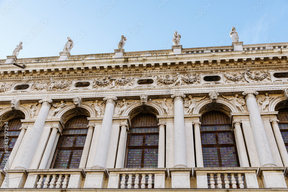 Obraz premium Venice, Italy - December 05, 2025: Architectural details of historic building facade with ornate columns and sculptures against a clear blue sky, showcasing Renaissance artistry and craftsmanship