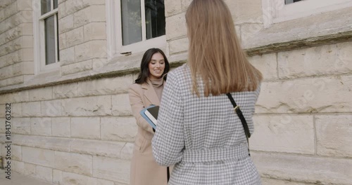 The moment of a meeting between two businesswomen near a white building in the city center, shaking hands with the intention of addressing important matters.