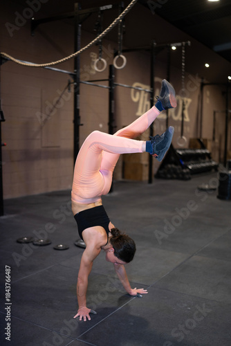 Athlete Displays Balance, Skilled Sportswoman Maintains Pose Amidst Gym Equipment And Concentration, Female Competitor Demonstrates Remarkable Flexibility And Poise During Freehand Inversion Exercise
