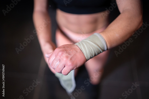 CrossFit Competitor Getting Ready For Exercise, Determined Woman Securing Wrist Strap For Intense Workout Session, Tattooed Female Athlete Diligently Wrapping Wrist And Applying Chalk Before Training