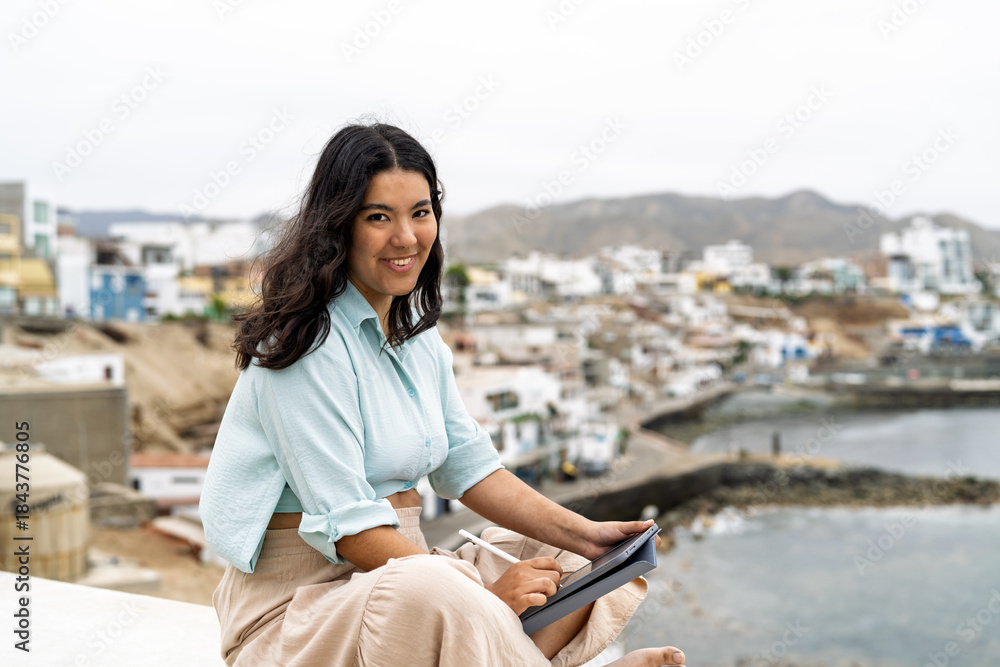 Fototapeta premium Young woman creating digital art with tablet by sea