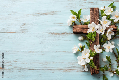 Rustic wooden cross decorated with white springtime cherry blossoms, resting on a background of weathered light blue wooden planks.