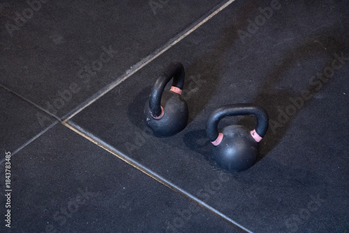 In a gym, two kettlebells can be seen sitting on the tiled floor