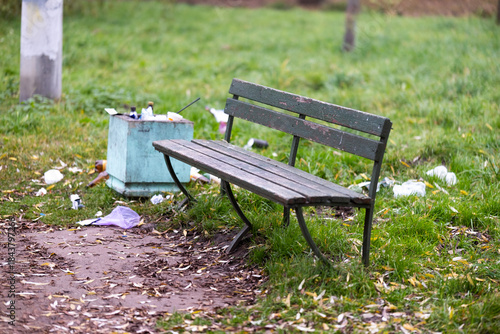 A trash can is positioned right next to a bench that is located in a park. High quality photo