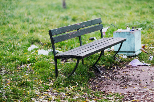 A trash can is positioned right next to a bench that is located in a park. High quality photo