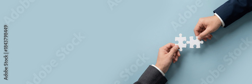 Hands connecting white jigsaw puzzle pieces on soft blue background for business partnership concept