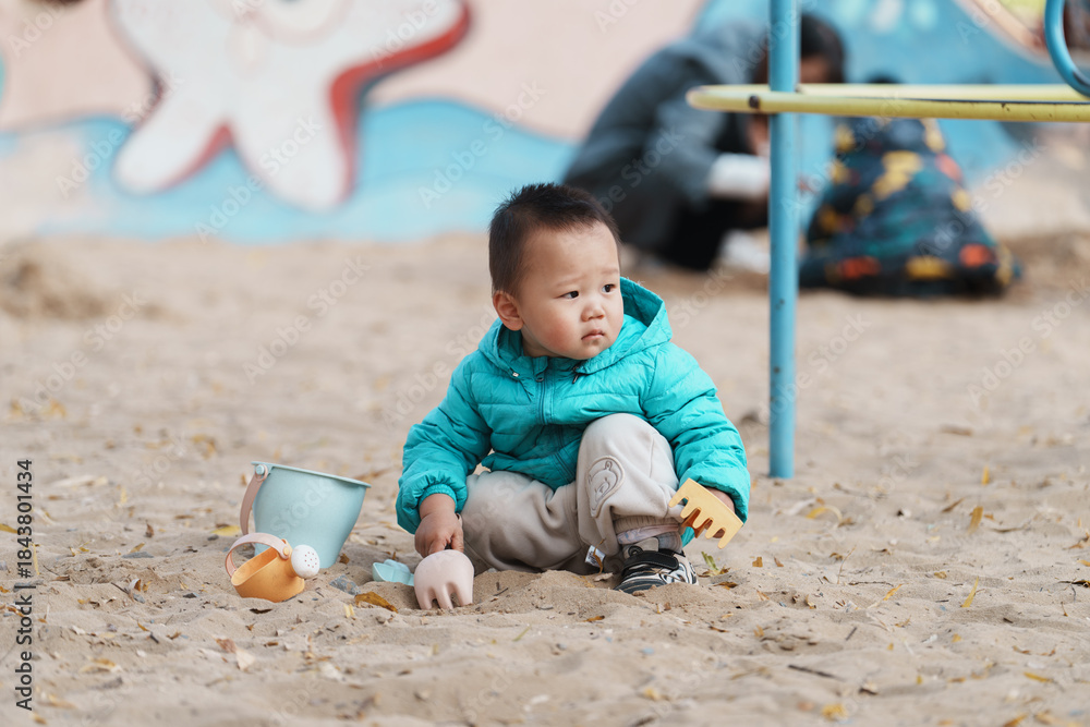 Naklejka premium An Asian boy playing in a sandbox at a playground in winter