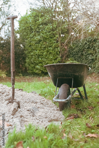 Construction work in the yard of a private home, a wheelbarrow a shovel and a pile of earth against the backdrop of a modern building 