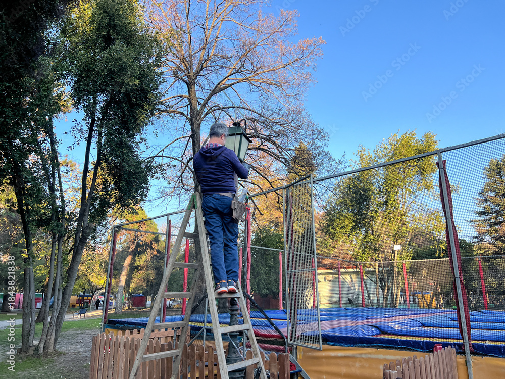 Ταπετσαρία Caucasian man standing on a ladder repairing a lamppost in an urban public park