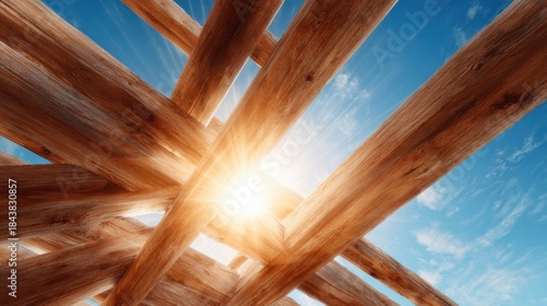 An intricate arrangement of wooden beams dramatically illuminated by sunlight against a clear blue sky, creating an inviting and warm architectural aesthetic.