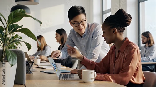 Two diverse colleagues collaborate closely over a laptop in a modern office setting reviewing data and strategizing for business success with focus and teamwork