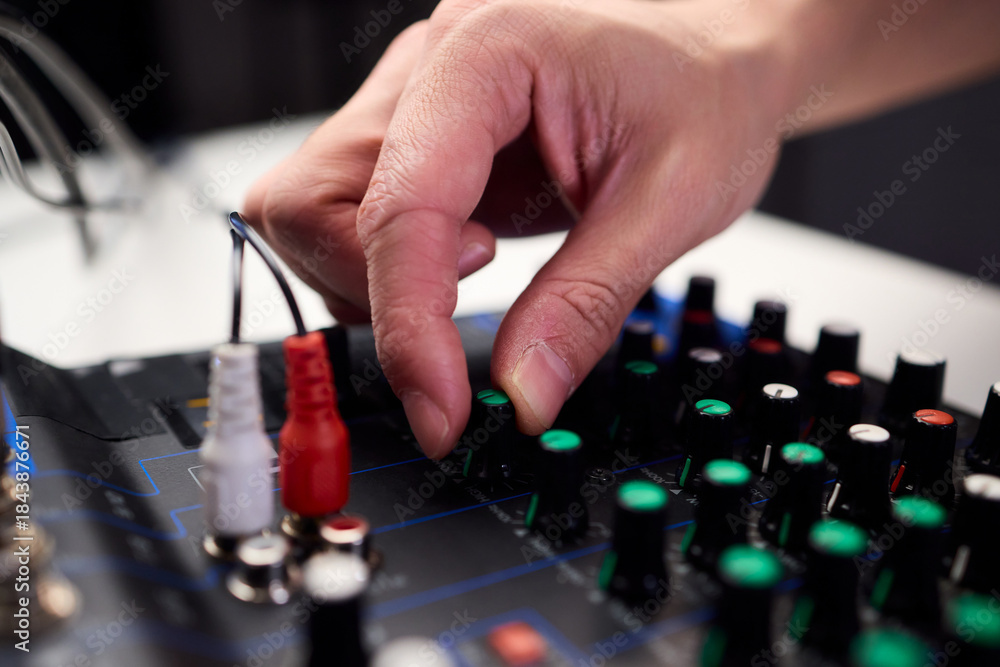 Fototapeta premium Closeup of hands adjusting mixer with glowing LED indicators and cables, Detailed image of operator controlling mixer dials and monitoring sound through sensors and LEDs