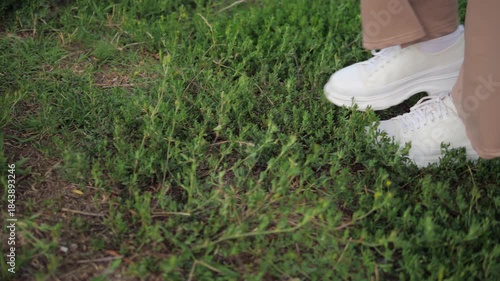 close-up of women's legs in white sneakers walking on grass
