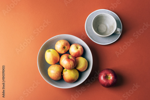 Fresh ripe apples in a bowl and an empty cup with saucer on an orange background. Top view, flat lay, copy space