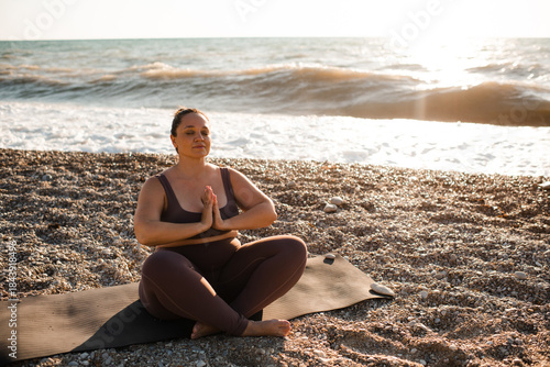 Woman 30-35 year old doing yoga stretching at beach over sea background outdoors. Healthy active lifestyle. Meditating.
