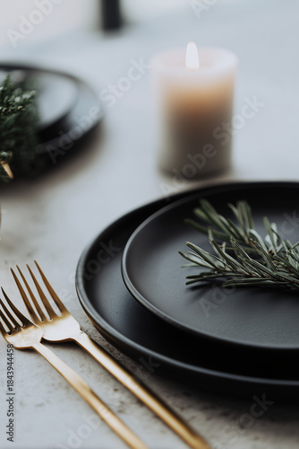 Minimalist holiday table with matte black plates, gold cutlery and a single candle