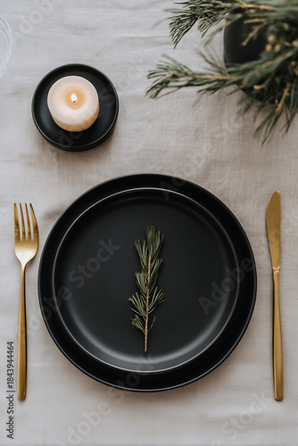 Minimalist holiday table with matte black plates, gold cutlery and a single candle