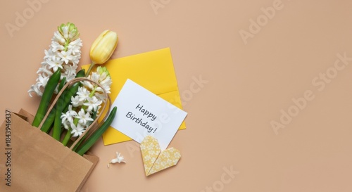 Birthday card with hyacinths and yellow tulip beside kraft bag on beige background