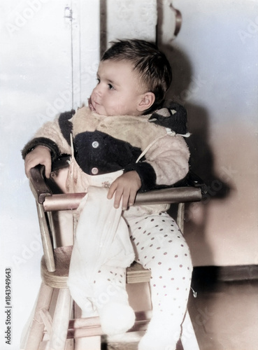 A vintage portrait of a one-year-old girl sitting in a high chair. Retro photo from 1995.